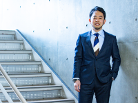 コンクリートの壁と階段の前に立つ千葉大学 堀田英之准教授の画像